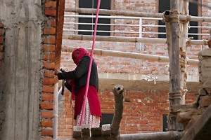 Sospesa ad oltre 10 metri di altezza dal suolo, questa donna Newari di casta "Sudra" lavora alla facciata di questo edificio in equilibrio instabile su questa impalcatura realizzata con le canne di bambù e senza alcun rispetto delle normative basilari di sicurezza, villaggio di Bungamati, Nepal 2018.