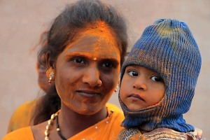 Ritratto di una donna Hindu con il suo bambino: entrambi ricoperti dalla polvere arancione della curcuma durante i festeggiamenti dedicati alla Dea Yallamma. Lei si chiama Himagouri, il bambino Ajatashatru. Entrambi appaiono molto tranquilli e rilassati nonostante la confusione che li circonda. Dintorni del villaggio di Saundatti, regione del Karnataka, India 2015.