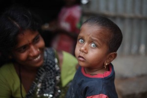 Charulekha, questa bimba Hindu dai bellissimi occhi verde smeraldo mi fissa incuriosita e quasi preoccupata: probabilmente non ha mai visto un bianco e, per giunta, "armato" di macchina fotografica. La sua mamma sorride divertita mentre la tiene amorevolmente in braccio. Entrambe sono arrivate sino al villaggio di Saundatti per essere presenti ai festeggiamenti in onore della Dea Yallamma (la Dea della Fertilità). Regione del Karnataka, India 2015.