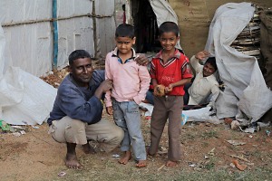 Aseem, il bambino sulla sinistra, pur abbracciato dal padre Bhaskar, mostra chiaramente il suo grande imbarazzo dinanzi all'obiettivo della mia macchina fotografica. Il bambino sulla destra (di nome Chandresh), invece, sorride divertito mentre il padre Abhik saluta cordialmente.Villaggio di Saundatti, regione del Karnataka, India 2015.