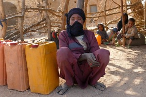 Ragazzo Haoussa siede accovacciato accanto ai bidoni che contengono l'acqua raccolta per gli usi domestici subito dopo l'alba, Villaggio di Dabaga, Niger 2020