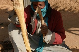 Uomo Haoussa modella un bastone di legno utilizzando uno strumento simile ad uno scalpello, Villaggiio di Dabaga, Niger 2020