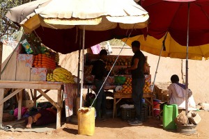 Banco di frutta a Niamey Est, il proprietario riposa sotto il bancone all'ombra, mentre il figlio serve un cliente, Niger 2020